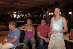 Foto 3: Hier sind Menschen beim Bowling und ein junge Frau im Rollstuhl hält die Bowlingkugel in der Hand,